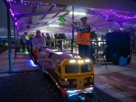 Miniature train at the station under lights with station master signaling to proceed