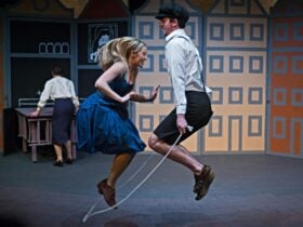 a young blond female wears a blue dress and jumps rope with a young man in white shirt and breeches