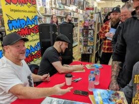 Two men sit at a table a line of people waiting to meet them