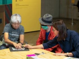 A photograph of 2 participants of Art by Description and a staff member using tactile resources