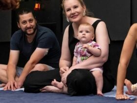 A photograph of 3 adults sitting on the floor, one is holding an infant