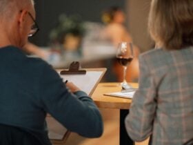 Two people drawing, with a glass of red wine on the table