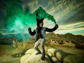 A man dressed as a rabbit in the desert. Green smoke is coming from a can in his hand.