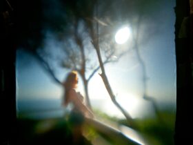A photograph of a woman standing at a lookout overlooking the beach, surrounded by trees
