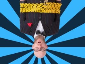 A man tied up in yellow chains, hanging upside down, in front of a blue striped background