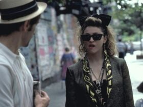 Woman walking towards man wearing 1980s style clothing, sunnies and big hair bow