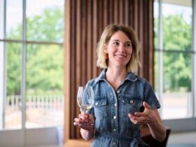 A woman holds a glass of wine and is gesturing with her other hand