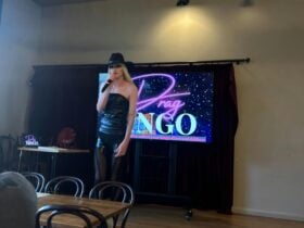 Shows a drag performer on a stage in front of a Drag Bingo sign