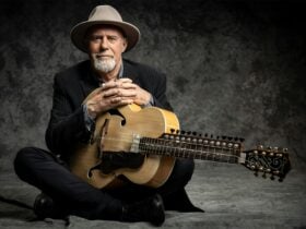 Harry Manx sitting down, holding stringed instrument