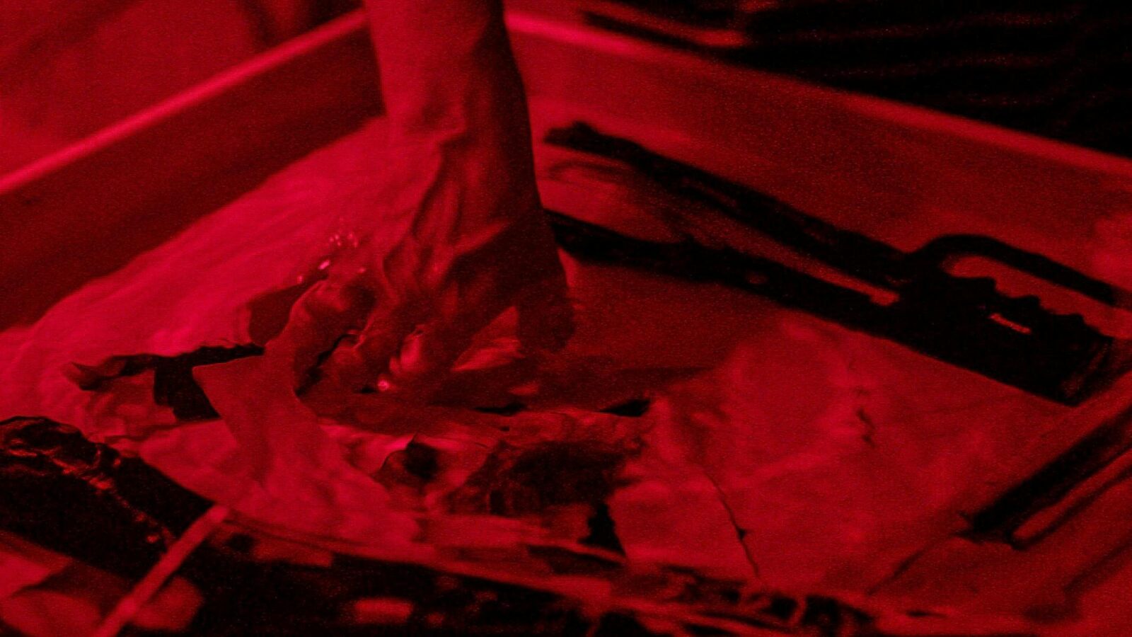 A photograph of a hand in a darkroom tray developing a photographic print