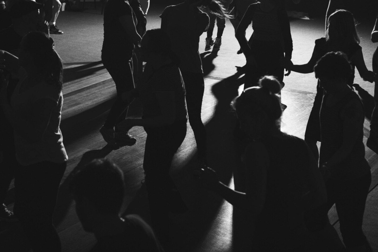 A group of silhouetted dancers on a dark dance floor