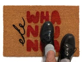 Image of a two feet standing on a door mat with the words 'ete wha nay nga' painted on the mat