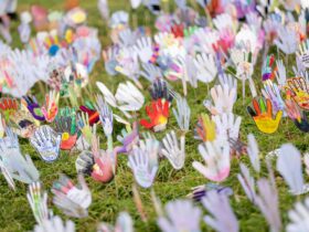 Colorful hand-shaped cutouts decorated with various patterns, mounted on sticks on grass area