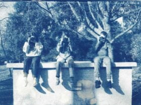 A cyanotype print photograph of three kids sitting on a ledge holding cameras up to their faces