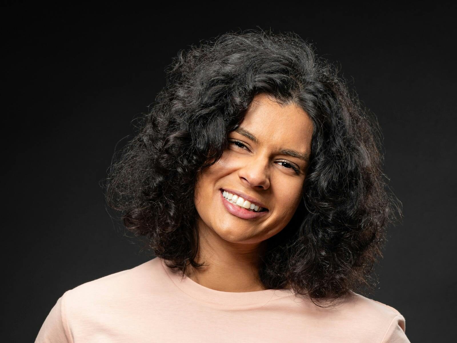 A woman smiling with curly hair in a pink shirt