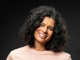 A woman smiling with curly hair in a pink shirt