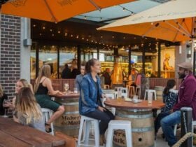 Customers seated outside at a bar with bright orange umbrellas and wooden tables.