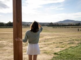 A tourist stands at a lookout, viewing vast open bush-covered fields stretching into the distance
