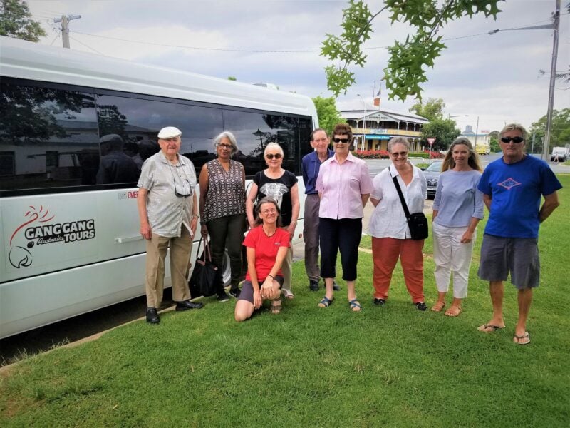 eight adults standing on grass in front of white tour bus