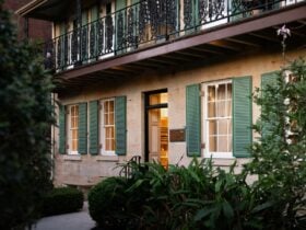 Sandstone heritage manor with green shutters, garden path, and lush surrounding foliage.