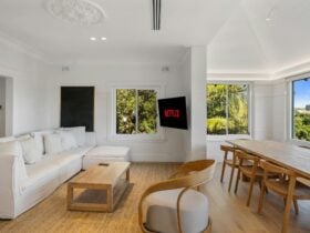 Living room with sofa, TV showing Netflix, and large windows framing harbour views and greenery.