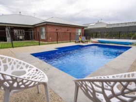 Pool area featuring 2 white charis, 2 sun lounges and some pool toys in the backyard. Pool is heated