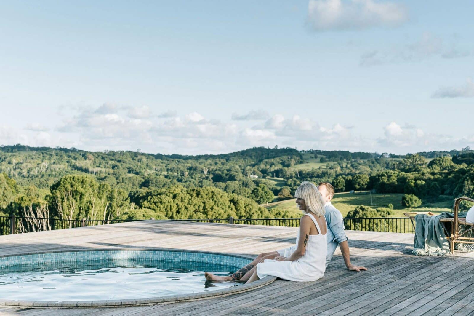 Couple sit on pool deck with their feet in the water gazing out to scenic rural vistas