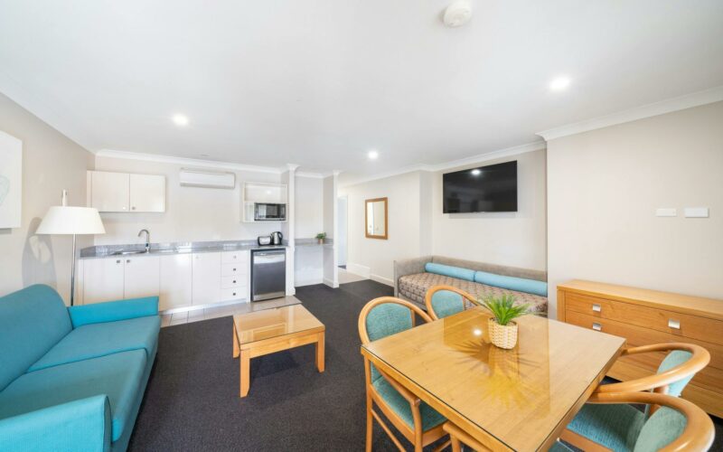 Stylish lounge room with fully equipped kitchen and dining area adorned with blue accents.