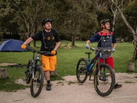 Two mountain bike riders walk past a tent at Ngarigo campground, Kosciuszko National Park. Photo: