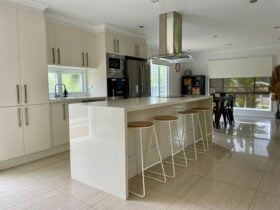 modern kitchen with four bar stools and a fully tiled floor. kitchen has a sink and a window.