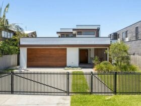 Image of front facade of home. Manicured lawns and a black metal fence in front of home.