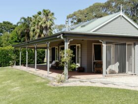 Country cottage in sage colour, with climbing rose, and wide shaded verandah