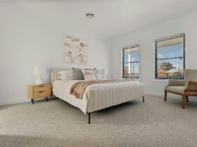 Main bedroom with king bed, carpet, side tables, 2 windows, armchair