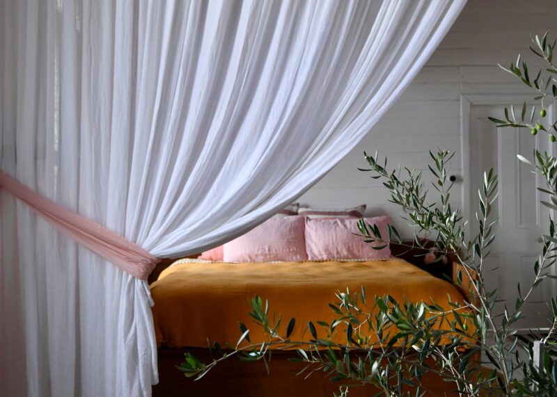 Linen curtain drawn back with a pink tieback to reveal a king size bed with French linen bedding