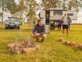 Man sitting around fire with caravan in background