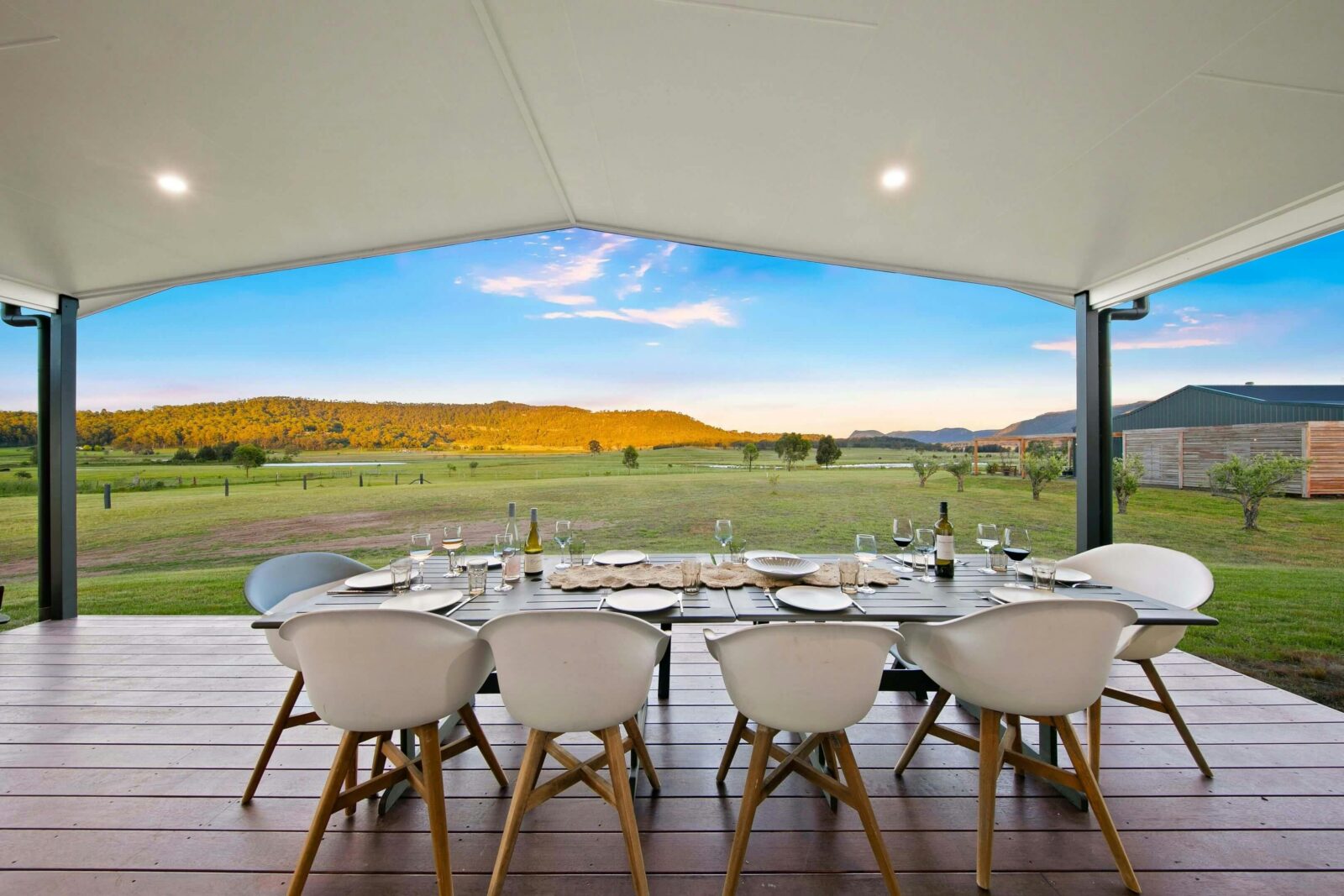 outdoor dining area with a long table set for eight overlooks a scenic landscape at sunset