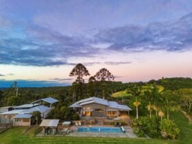 A large grey house with an outdoor pool and hot tub and a pastel sunset.