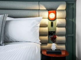A close-up of a hotel bed made with crisp white sheets with an upholstered bedhead and bedside table