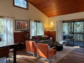 Inside cottage view of living room wirth comfy sofa, armchairs and table, looking towards the deck