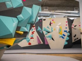 a photo of a vibrant climbing gym with teal wooden volumes and colourful holds