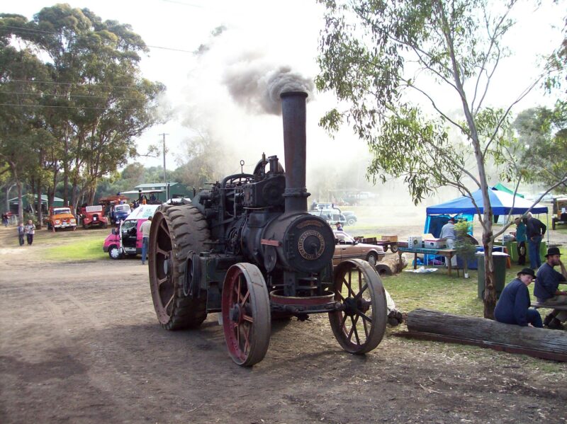 Old Large steam tractor with large rear and smaller front wheels bellowing smoke out of it