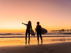 Surfers at sunrise with jetty in background