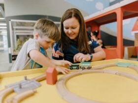 A young boy plays with the train set while a Discovery Space researcher supports. the experience.