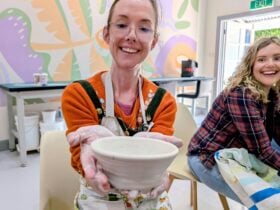 A student holds up the pot she has made on the wheel