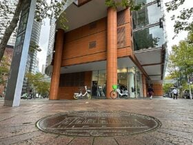 A photo of a plaque on a street with a large building and bikes in the background