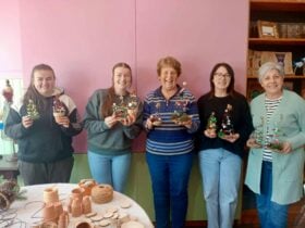 Guests standing in front of a pale pink background holding the Christmas Wire trees they have made