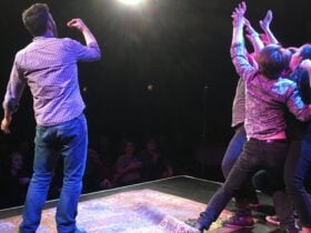 actors performing on stage with audience smiling watching