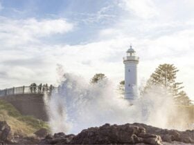 View of the Blowhole erupting with the Lightouse behind it and people watching on.h