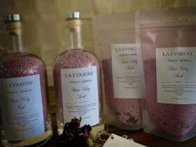 Pink bath salts in glass bottles and bags sitting on a wooden table