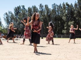 Multiple First Nations dances performing outdoors on the dance ground.